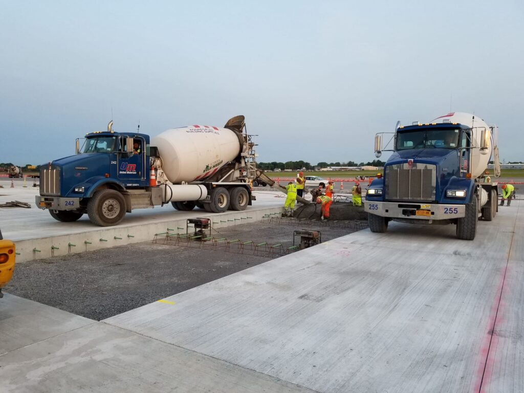 two United Materials trucks at a concrete pour in Western New York, with a crew in PPE busy laying concrete.